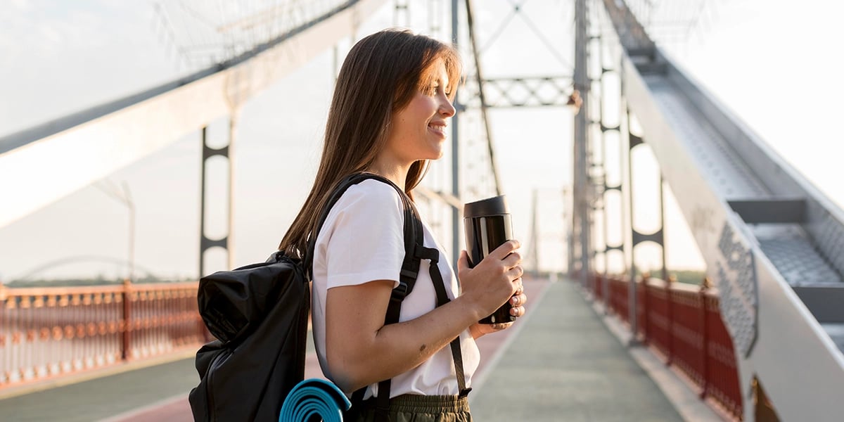 side-view-woman-traveling-happy-backpack-bridge-holding-thermos