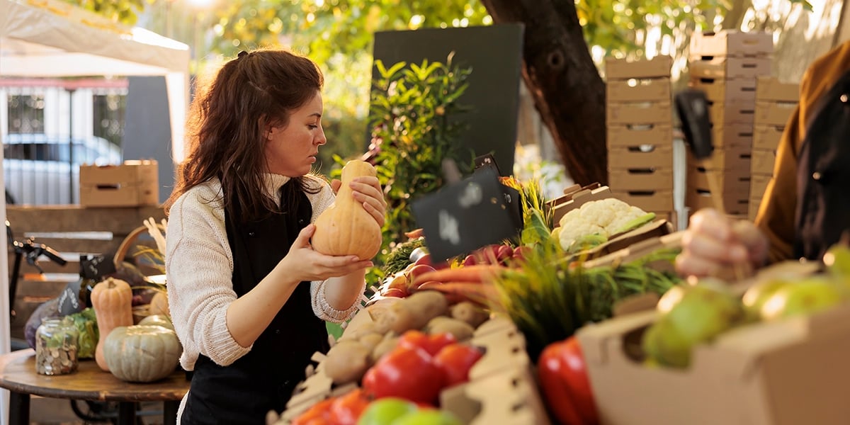 young-seller-arranging-fresh-natural-products-market-stall-farmers-wearing-apron-preparing-local-stall-fresh-organic-fruits-vegetables-outdoor-shop-selling-products- locally grown